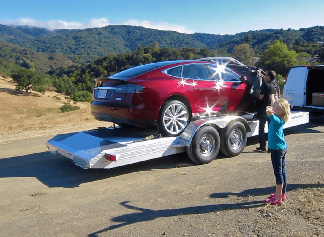 Car loaded on flatbed with family standing outside watching
